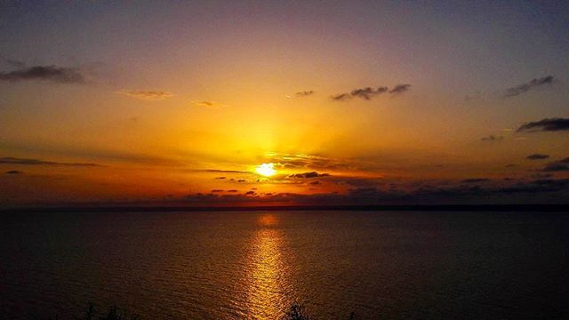 A serene sunset paints the sky with warm colors over the tranquil ocean waters, creating a peaceful coastal scene.