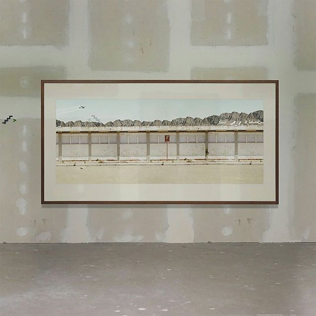 A framed photograph of a building and mountains hangs on a wall in an unfinished room.