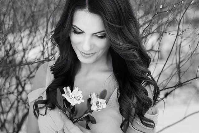 A woman gazes at flowers in a black and white portrait evoking softness and beauty.