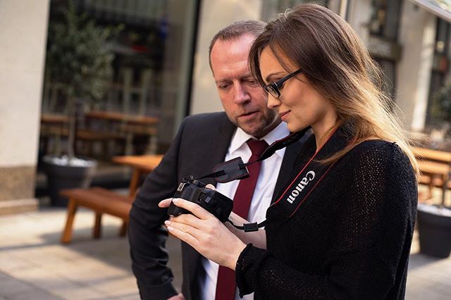 A man and woman are looking at a Canon camera outdoors, with the woman holding it.