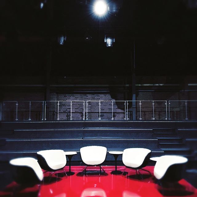 A modern stage setup with chairs, tables, and a red floor creates a minimalist and serene atmosphere.