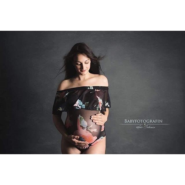 A pregnant woman poses in a floral bodysuit in a studio setting for maternity photos.