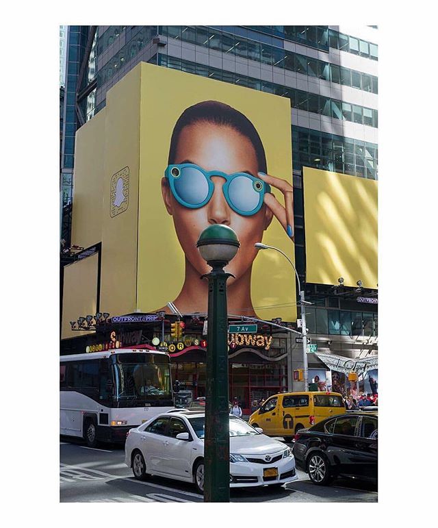 A vibrant billboard of a woman wearing sunglasses in Times Square surrounded by traffic.