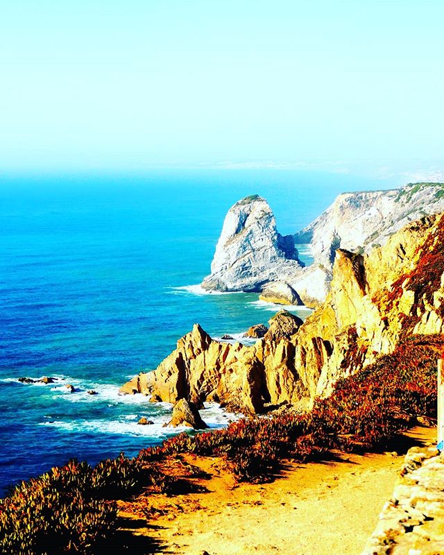 A scenic view of rugged coastline with cliffs, rock formations, and the ocean under a clear sky.