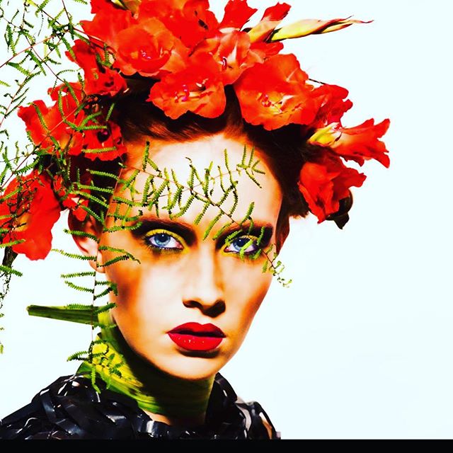 A woman wears a vibrant red floral headdress with green accents in a striking beauty editorial.