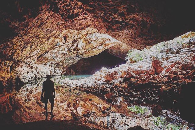 A man's silhouette stands in a cave with a pool, creating a mysterious and adventurous scene.