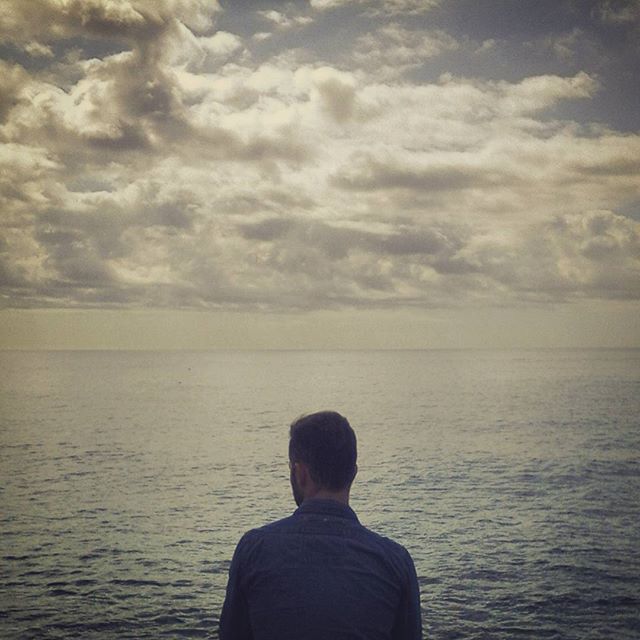 A man looks out over a calm ocean under a cloudy sky, capturing a moment of contemplation and serenity by the sea.