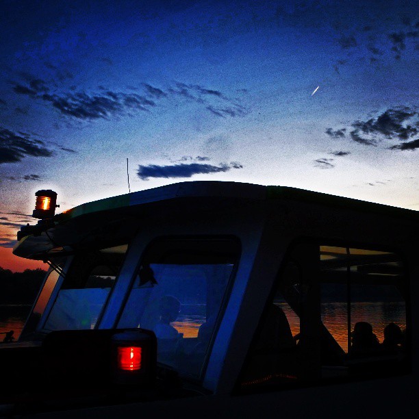 Silhouetted people aboard a boat navigate calm waters under a twilight sky.