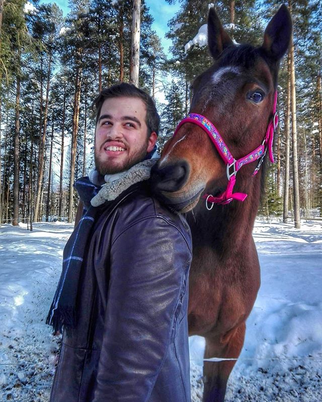 A smiling man poses with a horse in a snowy forest landscape in winter.