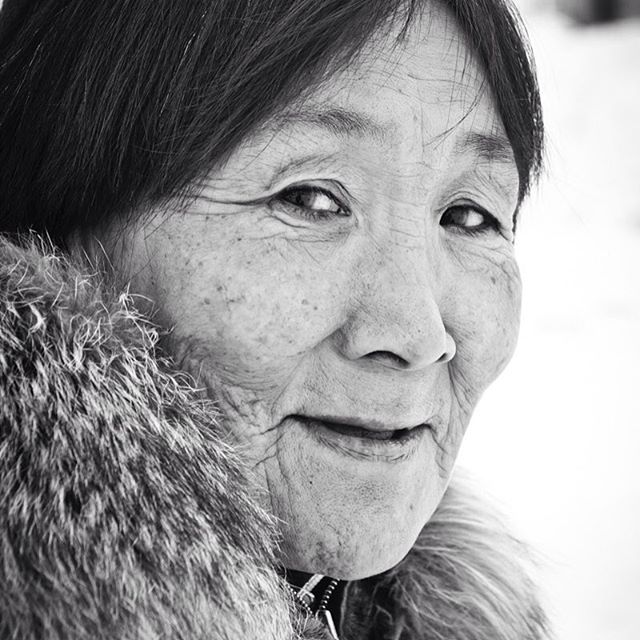 A black and white close-up portrait of an elderly indigenous woman with a warm, serene expression.