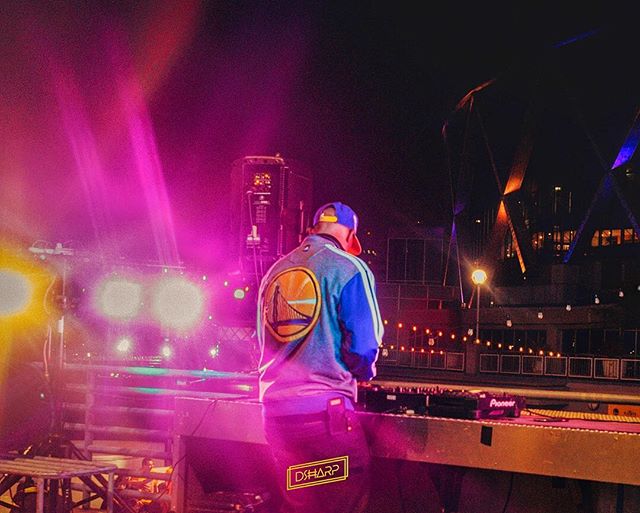 A DJ performs at a nighttime outdoor concert, bathed in colorful stage lights.