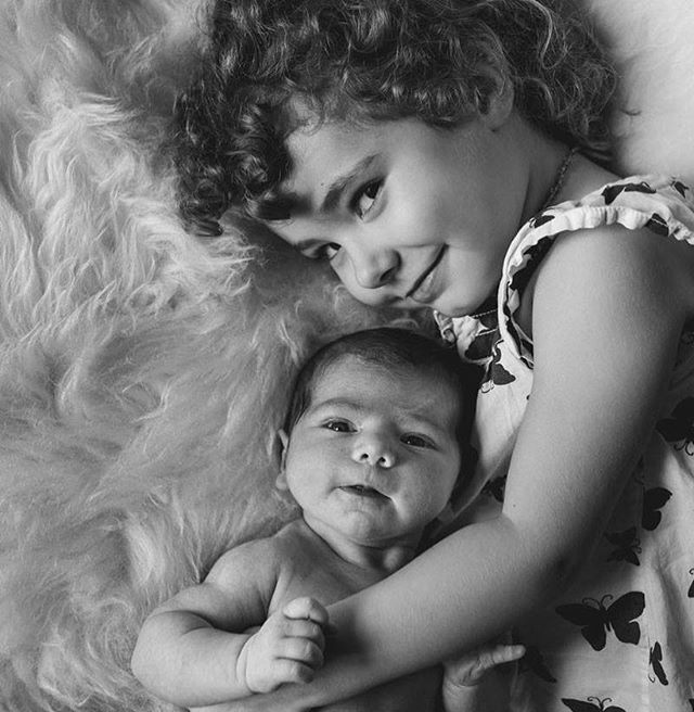 A baby and child are lying together in a monochrome close-up, showcasing a tender sibling moment.