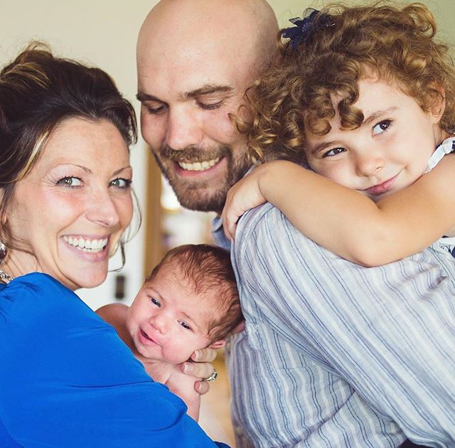 A smiling family of four, including a newborn, poses for a heartwarming portrait together.