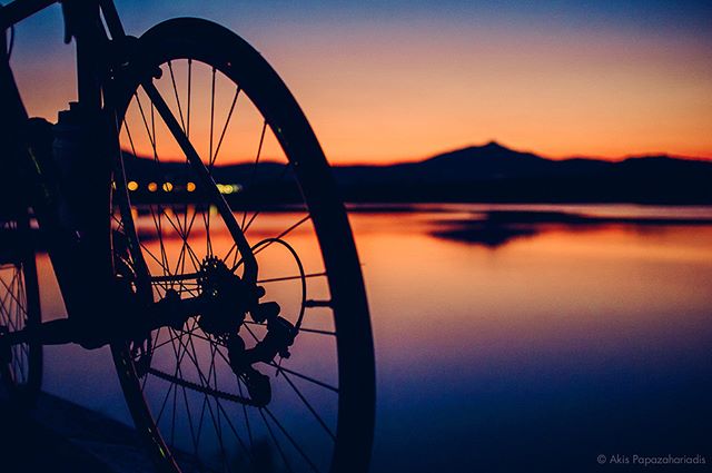 A bicycle wheel is silhouetted against a tranquil sunset over a calm lake, creating a serene fitness vibe.