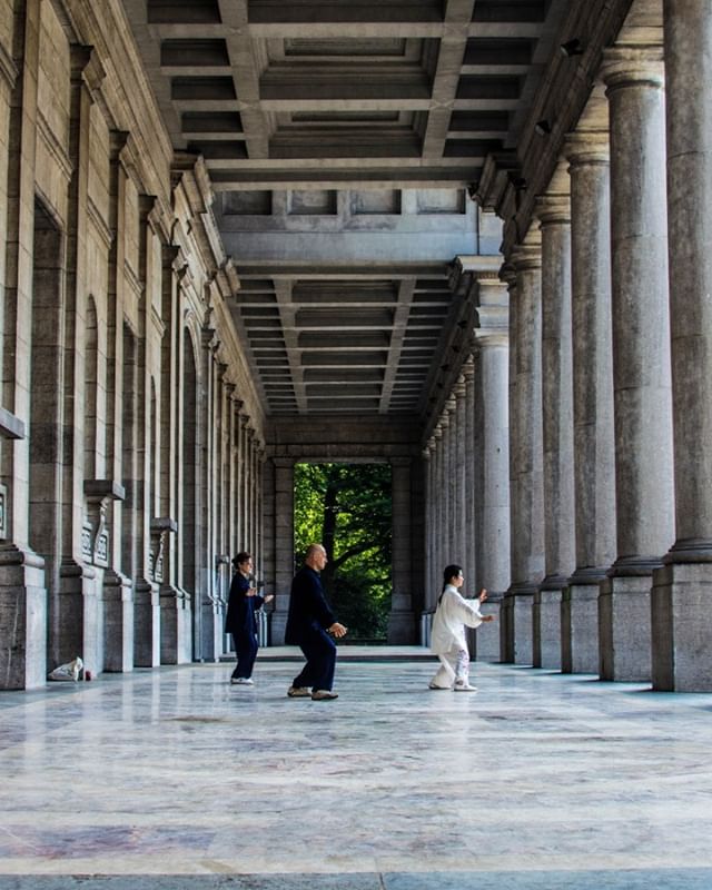 Three people practice Tai Chi outdoors in an arcade, promoting healthy lifestyles.