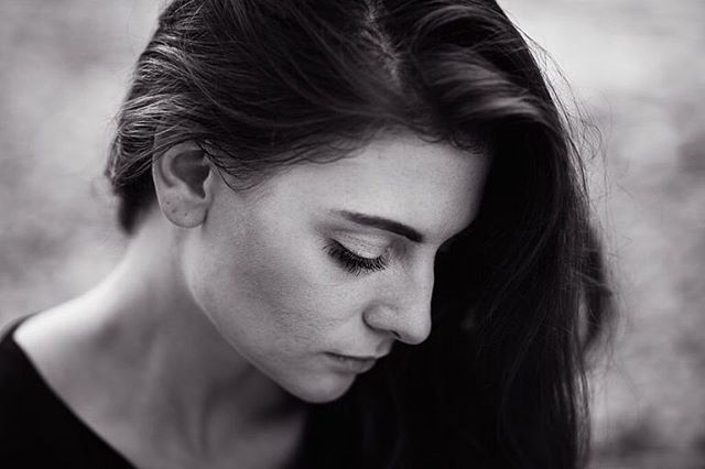 Monochrome portrait of a brunette woman looking down with soft, natural lighting.