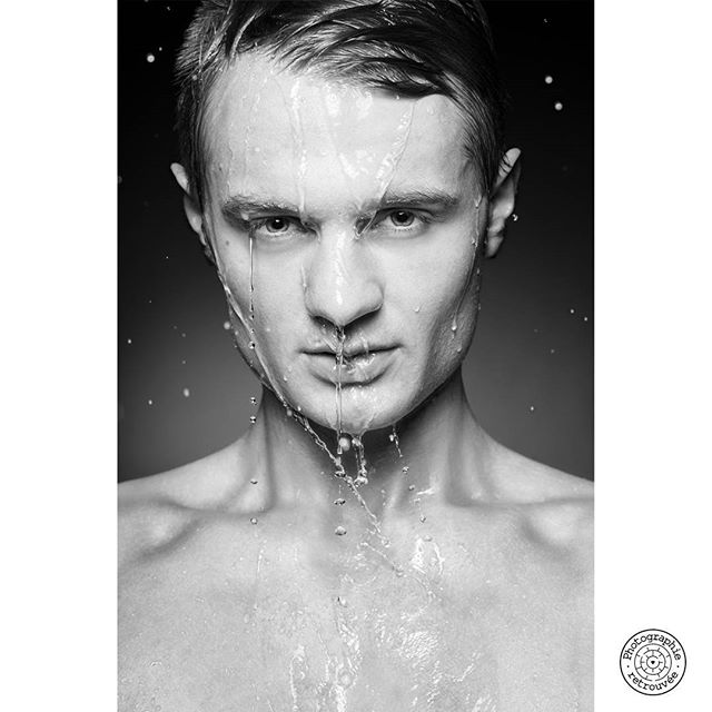 A striking black and white portrait of a man with water cascading down his face in a studio setting.
