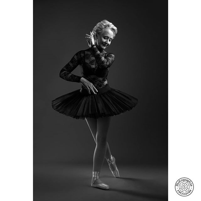 A graceful ballerina in a black tutu strikes a pose in a monochrome studio shot.
