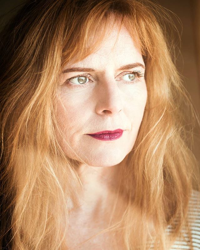 Portrait of a middle-aged woman with auburn hair looking thoughtfully away from the camera.