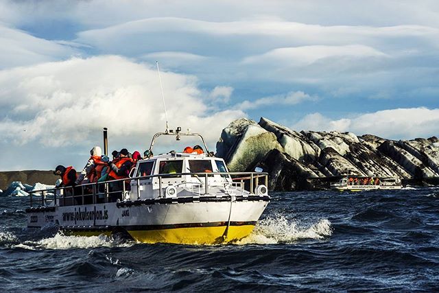 Tourists explore Jökulsárlón glacier lagoon in Iceland by boat, surrounded by icebergs under a partly cloudy sky.