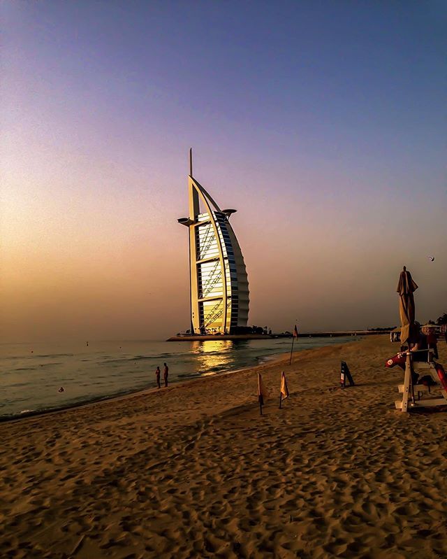 A scenic view of Burj Al Arab hotel on a beach in Dubai at sunset, perfect for travel and tourism advertising.