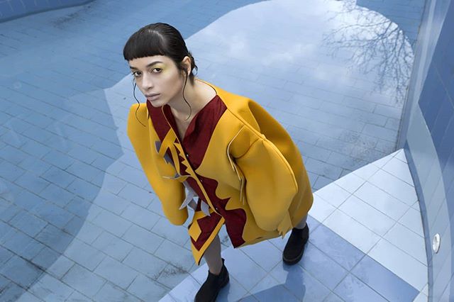 A woman models in a yellow and red outfit in a blue tiled pool area for a high fashion editorial.