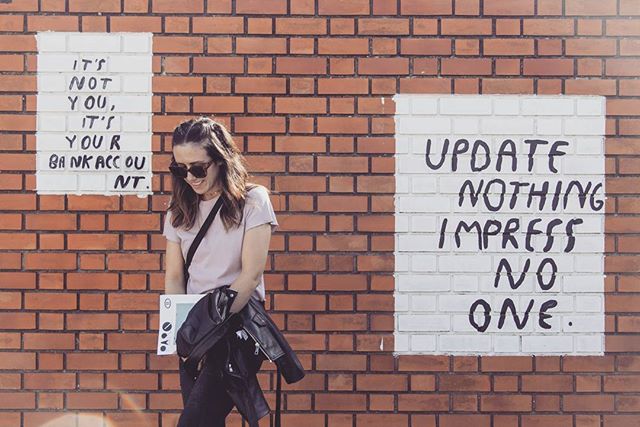 A smiling woman stands in front of a brick wall with graffiti art.