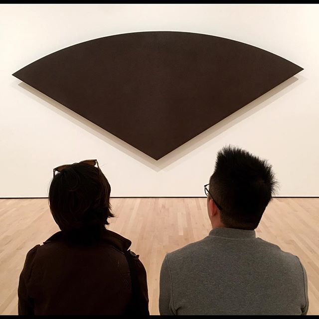 Two people view a minimalist brown artwork in a museum. Simple, modern art experience.