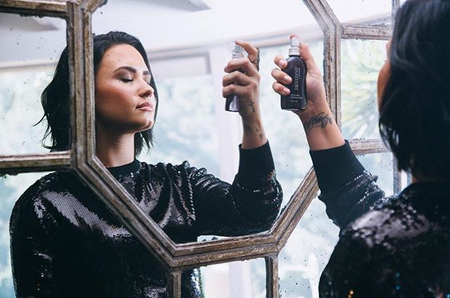 Demi Lovato looks at herself in the mirror while spraying DEVONNE product on her face for a commercial campaign.