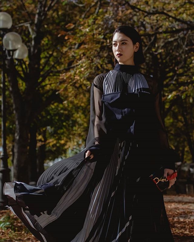 An elegant Asian woman in a flowing black dress walks in a park.