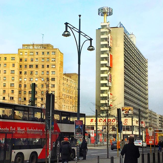 A vibrant urban scene features buildings, buses, pedestrians, and a vintage lamppost in a bustling city street in Berlin, Germany.