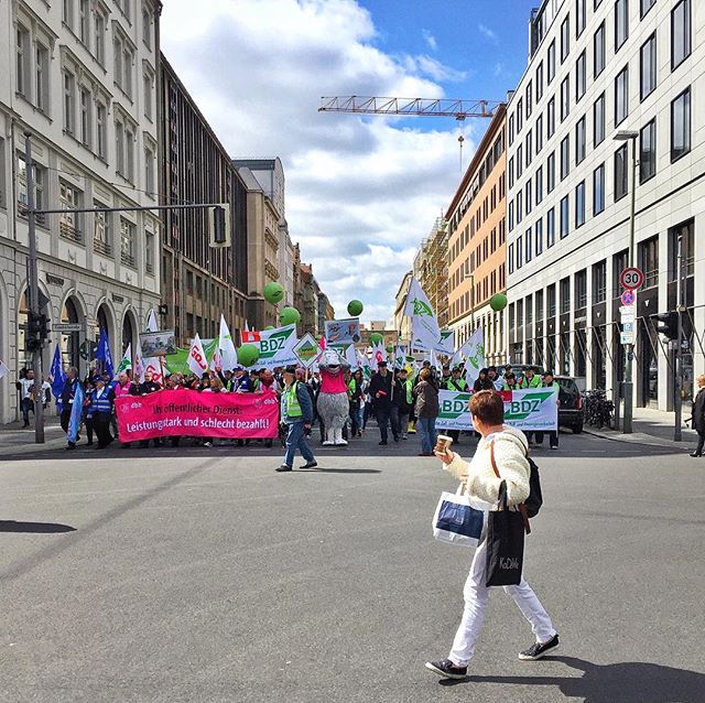 A large group of people march in protest down a city street with banners and flags.