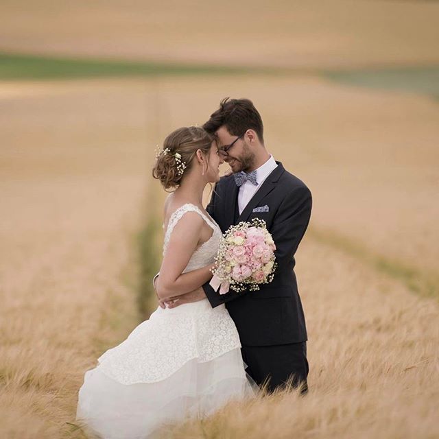 A bride and groom share an intimate moment in a golden field on their wedding day.