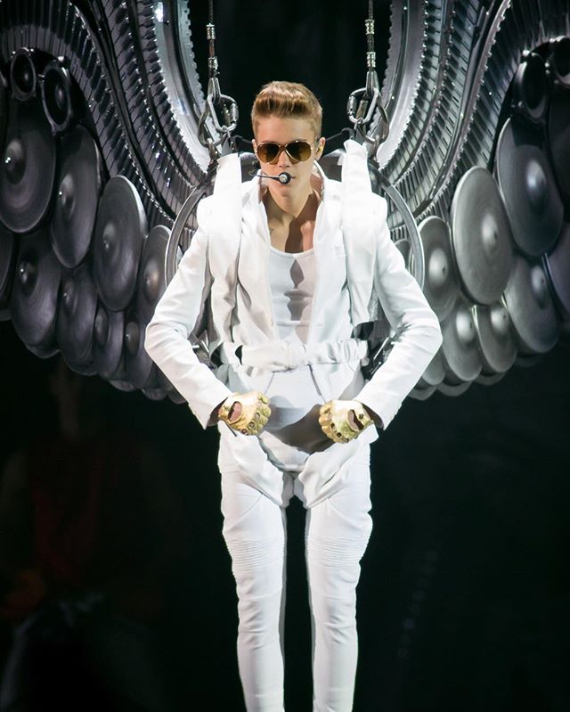 Justin Bieber performing on stage wearing a white outfit and wings in concert.