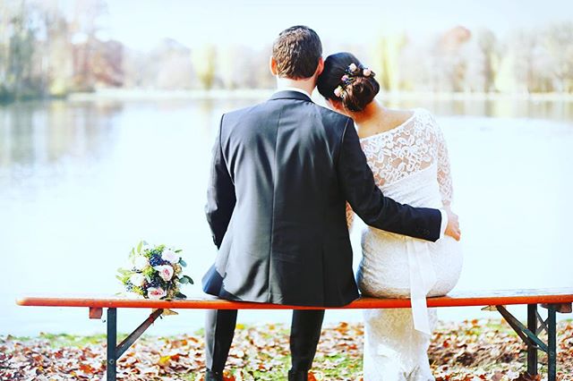 A newlywed couple sits on a bench by a serene lake, embracing the start of their married life.