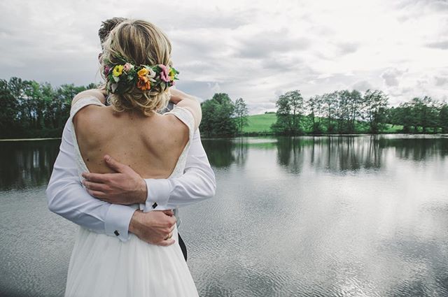 A bride and groom embrace by a calm lake, showcasing a dreamy and intimate wedding moment.