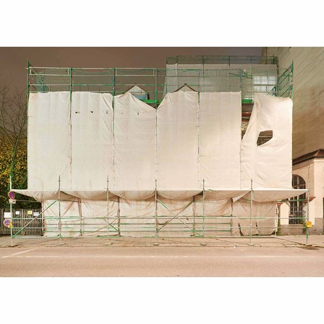 Building under renovation covered with scaffolding and white sheets on a city street.