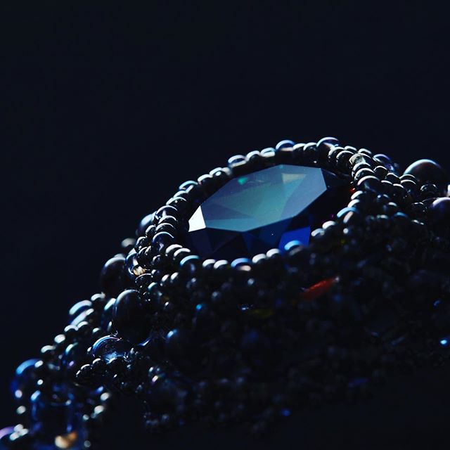 A close-up of a blue gemstone ring surrounded by dark beads, capturing luxury and sophisticated elegance.