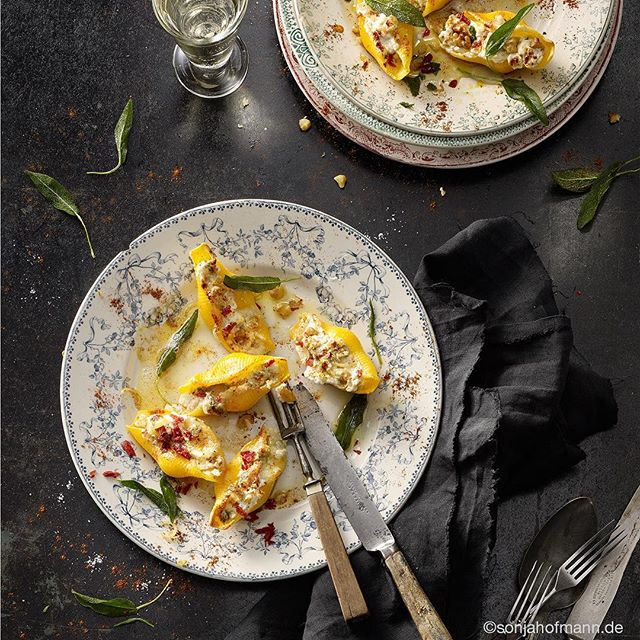 Overhead shot of stuffed pasta shells with sage leaves on a patterned plate for a rustic gourmet meal.