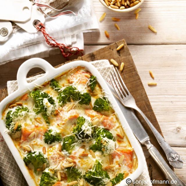 A delicious salmon and broccoli casserole topped with pine nuts on a rustic wooden table. 