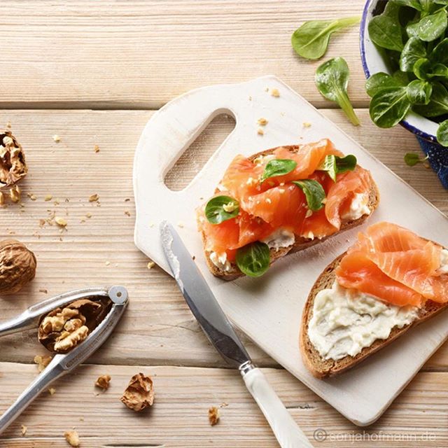 Two slices of bread topped with cream cheese and salmon, served with walnuts on a wooden surface. 