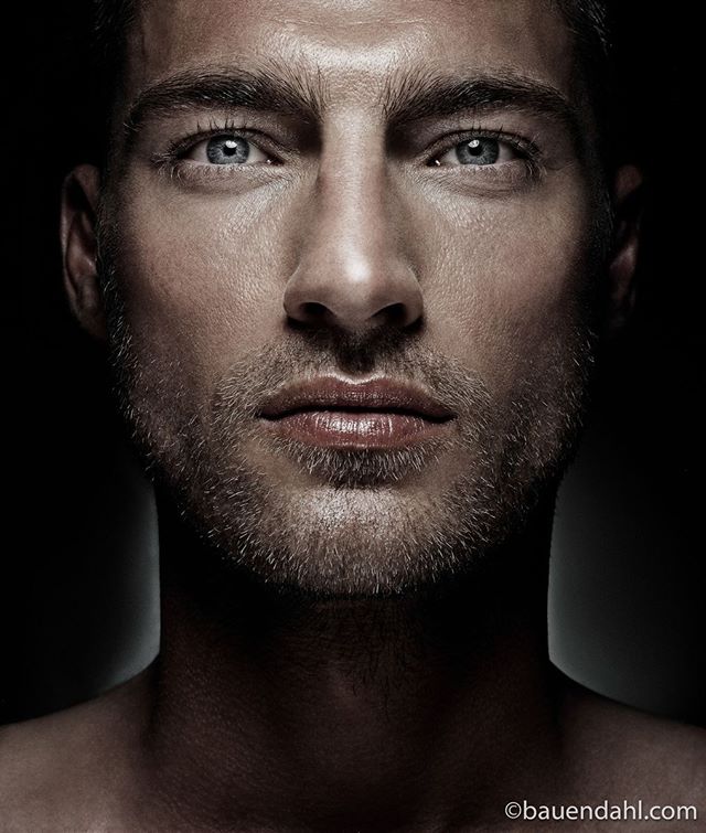 A close-up portrait of a handsome man with blue eyes against a dark backdrop, suitable for beauty and fashion advertising.