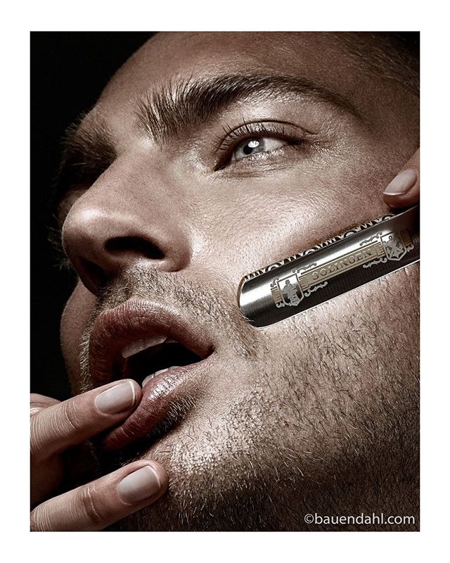 Close-up of a man shaving with a straight razor for grooming and skincare, showing the detail in his skin.
