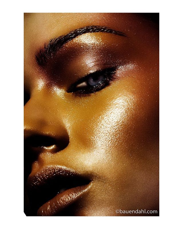 Close-up of a woman's face with glowing skin, featuring editorial makeup and dramatic lighting.