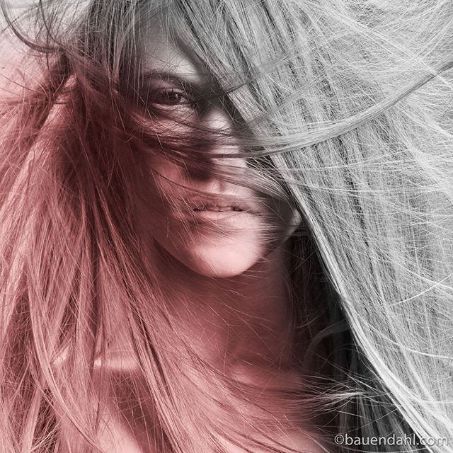 An artistic monochrome portrait of a woman's face partially obscured by flowing hair.