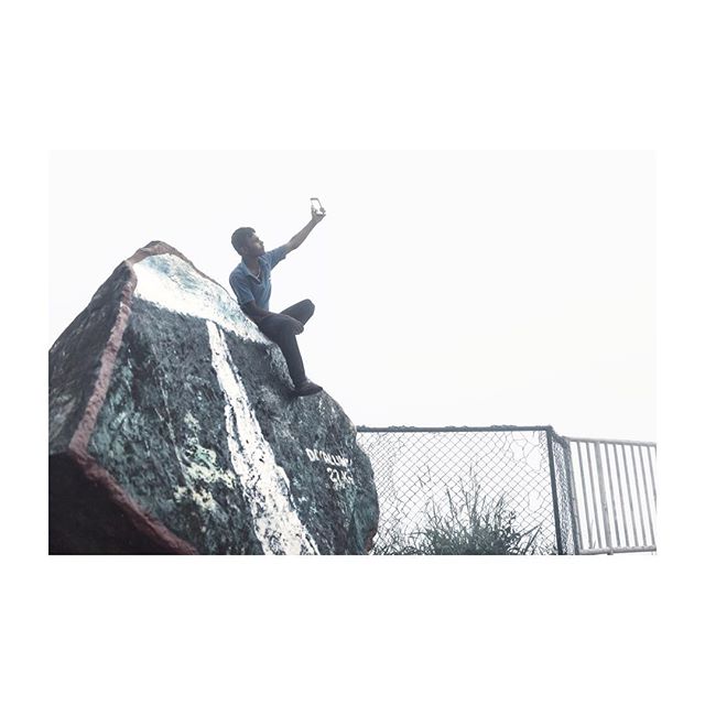 A man takes a selfie on a rock on a mountain top, enjoying the scenic view.