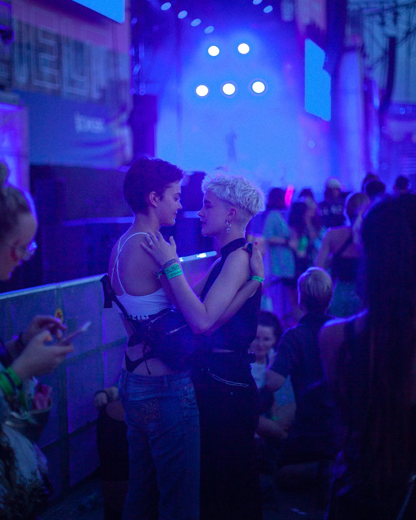 A couple dances closely at a concert in a lively, blue-lit atmosphere, surrounded by a crowd of people enjoying the event.