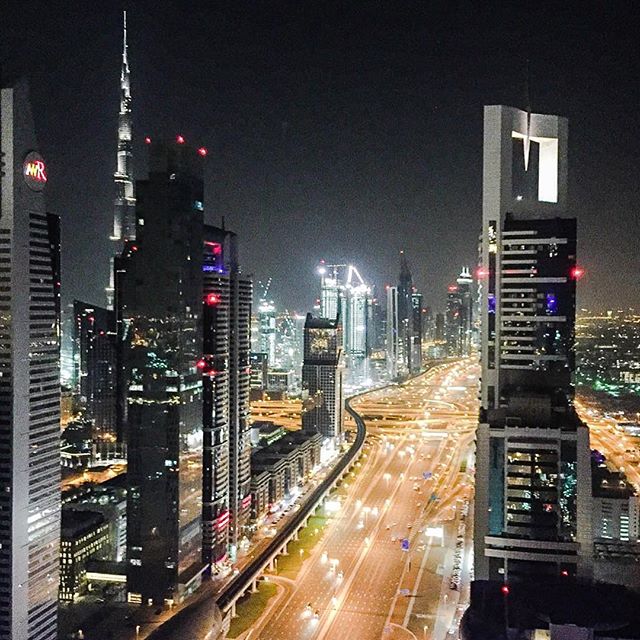 Aerial view of Dubai's illuminated skyscrapers and highways at night, showcasing its modern urban landscape and vibrant energy.