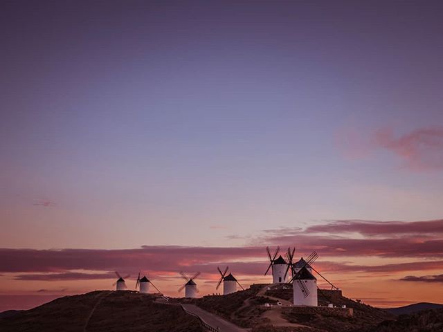 Scenic windmills on a hilltop at sunset, capturing a tranquil, rural landscape under a colorful sky.