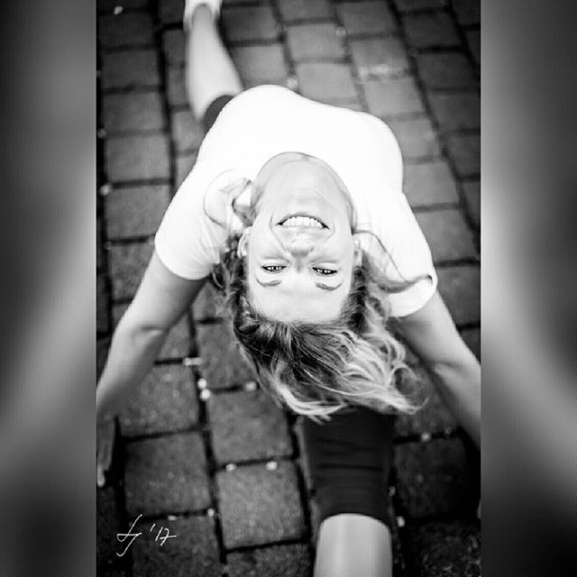 A smiling woman stretches outdoors in black and white, looking up at the camera with a cheerful expression.